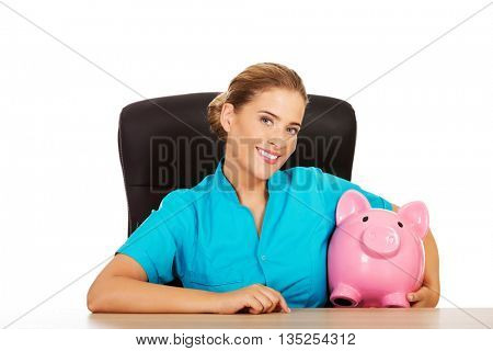 Young female doctor or nurse holding piggybank