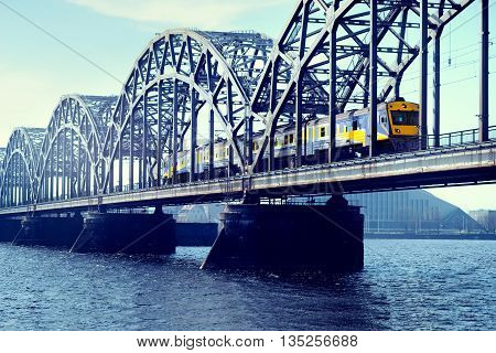 Blue with yellow electric train rides on the railway bridge over the river Daugava in Riga