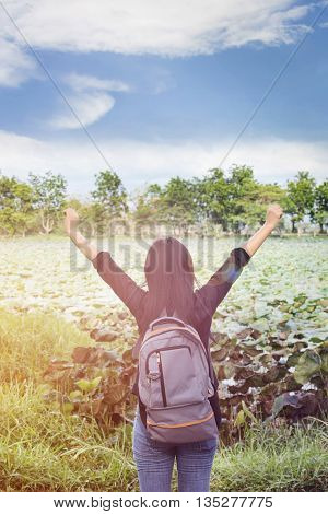 Women back or rare view with focused backpack on natural pond and puffy clouds sky view women raise or stetch two arms relax at the pond