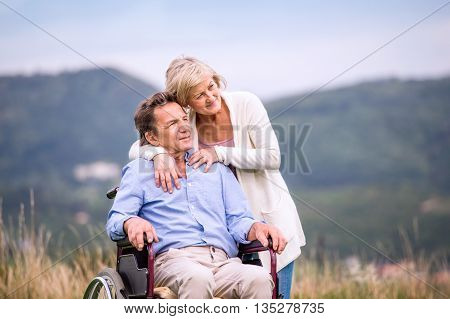 Senior Woman Pushing Man In Wheelchair, Green Autumn Nature
