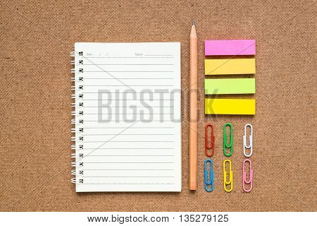 Group of colorful stationery tools - spiral open line notebook brown pencil colorful sticky note colorful paperclips - on brown background - education and business tool and equipment