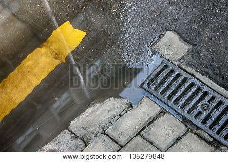puddle on road at drainage metal grill of drainage tray on sidewalk