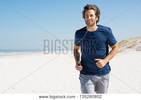 Mature man listening to music while jogging on the beach. Runner working out wearing earphones listening to music playlist. Man listening to music with mp3 player in armband and jogging at beach.