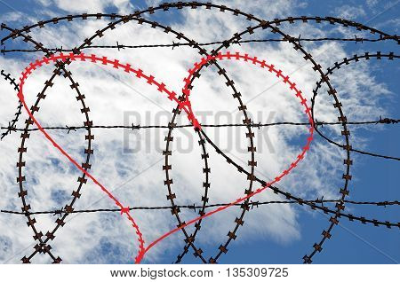 Barbwire fence with natural heart shape (digitall coloured red) on sky background. Love, freedom, peace and compassion concepts