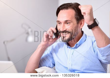 Thats amazing. Excited bearded man smiling and doing a sign of victory with hands while talking on the phone