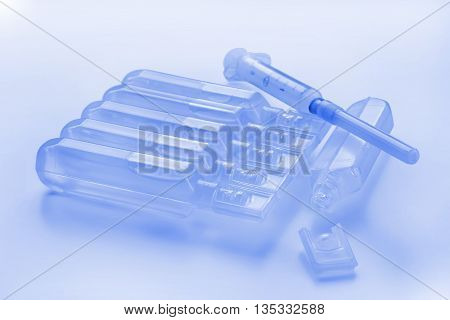 Plastic modern style ampules and syringe. Blue toned still life.