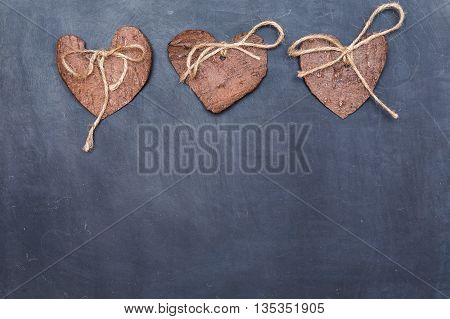 Three (3) decorative hearts made from tree bark on chalkboard, positioned above the middle of the photo. Hearts decorated with eco twine. Eco decor. St. Valentines greeting card idea. Handmade design.