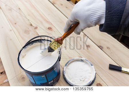 Holding painting brush in the jar with the white paint. Painting timber boards outside with the white paint or white coloured emulsion using 2 inches painting brush.