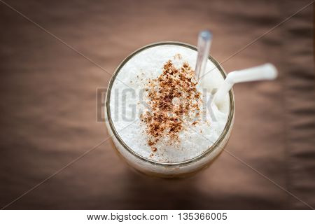 Iced coffee with microfoam on brown table mat; overhead view