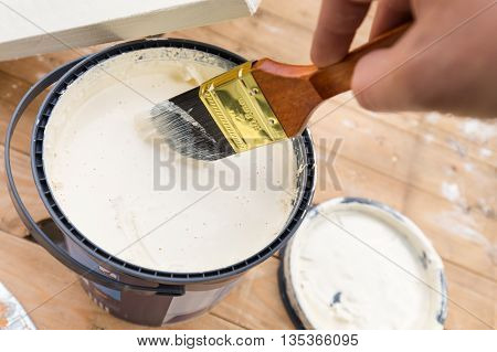 Holding painting brush in the jar with the white paint. Painting timber boards outside with the white paint or white coloured emulsion using 2 inches painting brush.