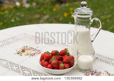 Bowl of strawberries standing on the table with glass of milk. Jug full of milk beside bowl of strawberries. Summer breakfast. Summer desert. Picnic idea. Healthy option