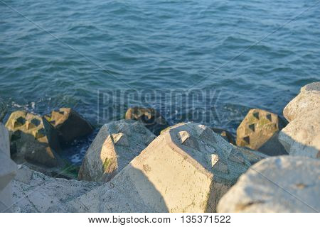Close Up Of Breakwater Made Of Concrete Tetrapods In The Sunset, With The Calm Sea In Background. Se