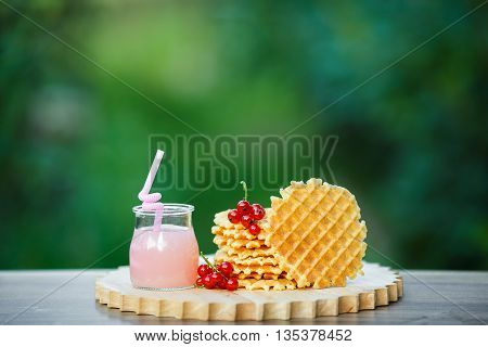 Belgian waffles with fresh berries on cutting board on background of green bokeh. grapefruit juice. pink cocktail with a straw.