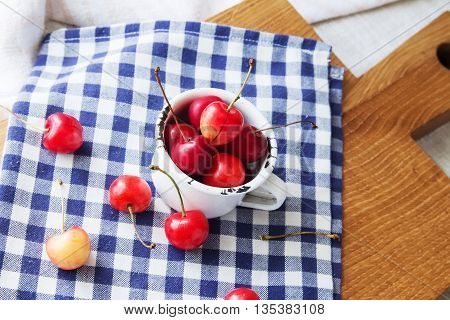 Composition of cup and berries. Cherries is the reason of the longevity . White retro cup and berries on a checkered napkin on the table. Retro cup and berries on a wooden cutting board