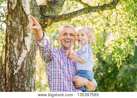 Young father with his son spending time in the park. Father pointing somewhere.