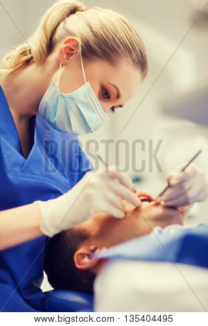 people, medicine, stomatology and health care concept - female dentist with dental mirror and probe checking up male patient teeth at dental clinic office