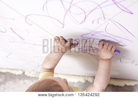 Baby boy drawing with wax crayon on plasterboard wall. High angle view