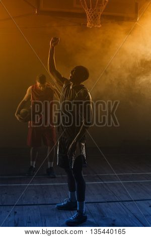 Victorious basketball player raising his arms up while his rival looking down