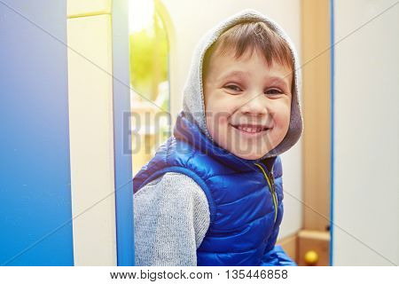 Small boy is sitting on a playground on a sunny day and smiling at the camera