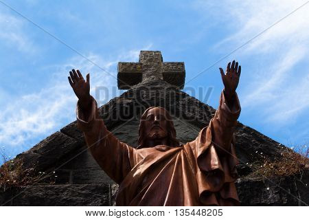 The statue in front of the Saint Rose Church with a cross and cloudy skies in the background in Santa Rosa California.
