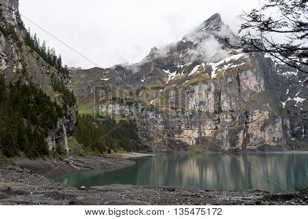Swiss lake Oeschinensee with waterfall and mountains in the clouds.