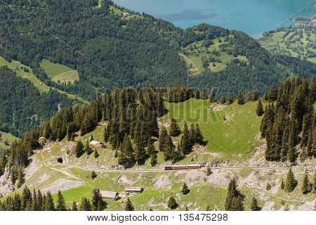 Cog Railway goes to tunnel with Thunersee on background of blue lake.