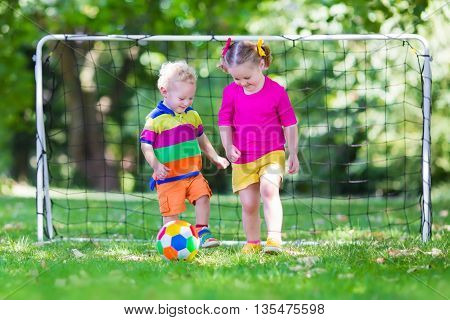 Two happy children playing European football outdoors in school yard. Kids play soccer. Active sport for preschool child. Ball game for young kid team. Boy and girl score a goal in football match.