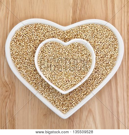 Quinoa grain health food  in heart shaped porcelain dishes over beech wood background. Salvia hispanica.