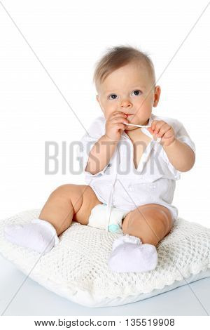 cute kid in whight blouse and diaper, the full-lenght sitting on a pillow and sucks a finger white background, isolated