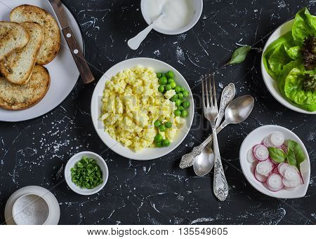 Ingredients for breakfast toast - egg's scramble toasted bread radishes green peas. On a dark stone background. Delicious healthy food