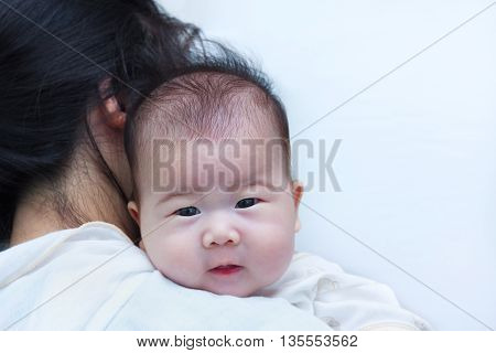 Mother and baby. Lovely girl resting on her mother's shoulder. Asian baby looking at camera.