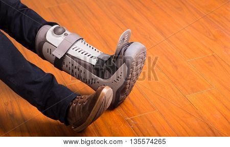 Big difference, one normal feet and other with orthopedic boot after an injury, wooden floor.
