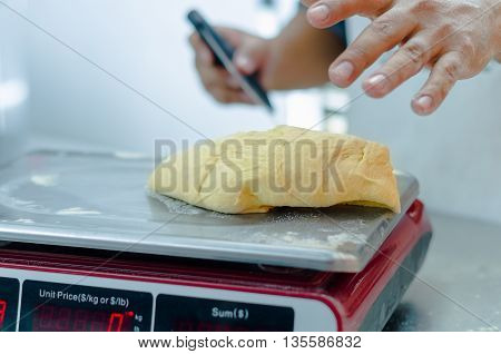 Bakers hands working and weighing bread dough on digital scale .