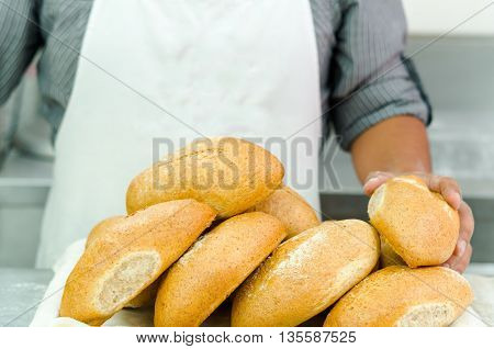 Pile of fresh bread loafs, baker standing behind with only apren and arms visible, bakery concept.