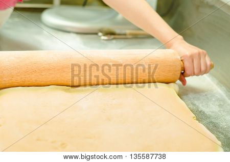 Bakers hands using large rolling pin working on bread dough.