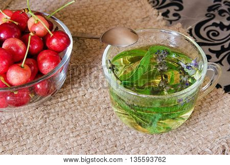 Herbal tea with mint and thyme on rustic table as well as fresh cherries