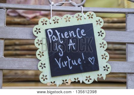 A philosophical Patience is a Virtue sign attached to a bench.