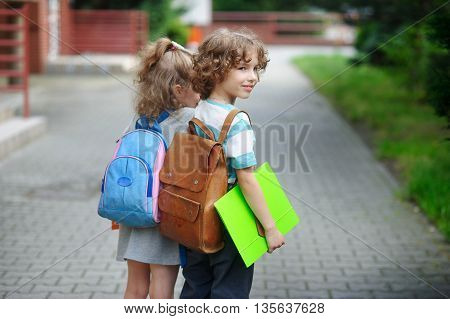Two little pupil of elementary school boy and girl stand having joined hands. The boy with a smile looks somewhere. It costs in a half-turn to the camera.