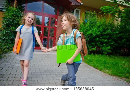 Two pupils of elementary school boy and girl on a schoolyard. They play pranks. Children have a good mood. They laugh.