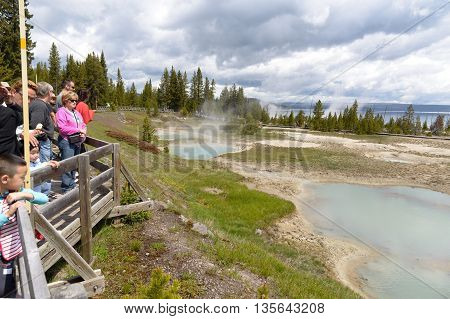 Yellowstone United States - May 31 2015: Clear aqua hot spring with deep central hole steam and limy shoreline people on boardwalk West Thumb area of Yellowstone National Park Wyoming.