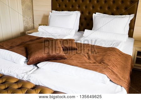 Luxury king-size brown and white bed with an upholstered headboard throw rug and cushions and footstool at the end close up view