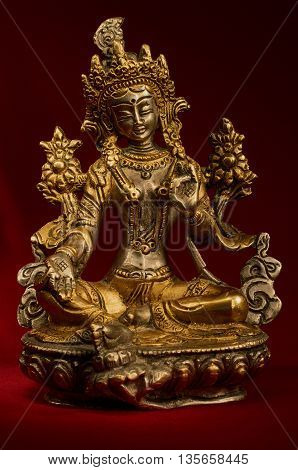Statuette of Green Tara on a red background. Vajrayana deity quick to help and protection. Om tare tuttare ture soha.