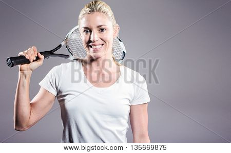 Portrait of female tennis player posing with racket against grey background