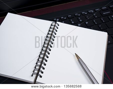 White blank notebook and pen on laptop keyboard (Selective Focus)