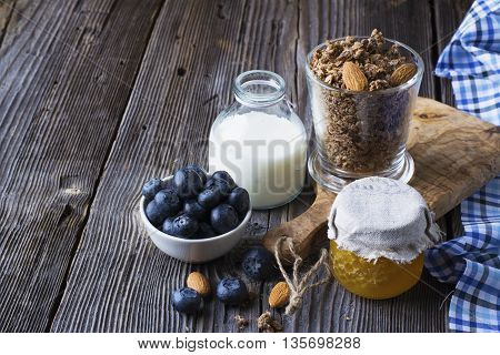 Healthy breakfast ingredients. Cereal, chocolate muesli, fresh blueberries, jar with honeycombs, rustic milk bottle on a simple plank dark background in rustic style. selective focus