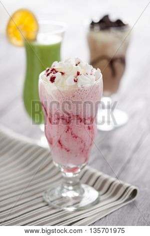 Sweet red berries cocktail with whipped cream and crashed meringue served in long glass. Fresh desserts composition with chocolate shake and kiwifruit mousse on the background.