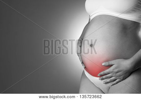 Caucasian pregnant woman in white lingerie with abdominal pain on gray studio background. Pregnancy concept