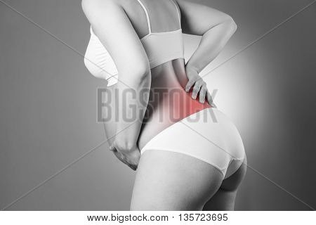 Caucasian pregnant woman in white lingerie with back pain on gray studio background. Pregnancy concept