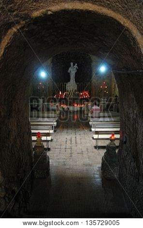 Mellieha, Malta - September 29, 2013. Interior of the Grotto of the Madonna in Mellieha set deep in a cave lit by flickering candles, with statue of the Madonna, benches and people. The Grotto is located beside a spring with waters that are reputed to hea