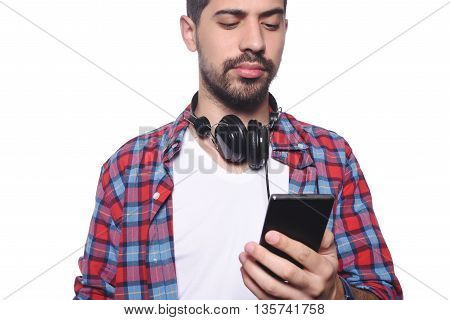 Portrait of a young latin man typing on his smartphone and using black headphones. Isolated white background.